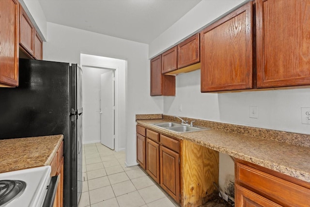 kitchen featuring brown cabinetry, freestanding refrigerator, a sink, and light tile patterned flooring