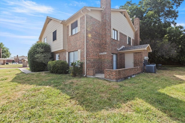 view of side of property featuring a chimney, brick siding, a yard, and central AC unit