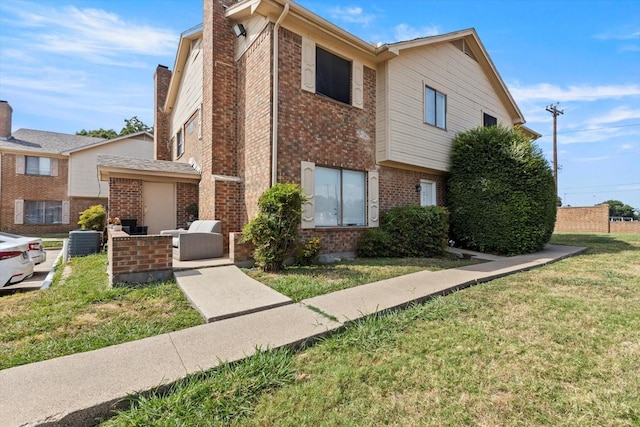 view of front of property featuring a chimney, a front lawn, brick siding, and central air condition unit