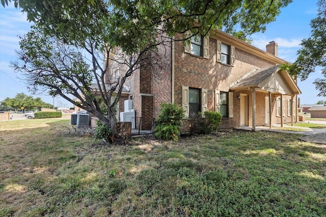 view of front of property featuring brick siding, central AC, a chimney, and a front lawn