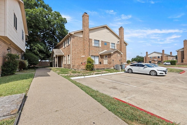exterior space featuring a chimney, brick siding, and uncovered parking