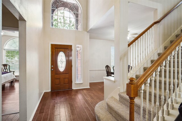 foyer with stairway, a high ceiling, a ceiling fan, and dark wood-style flooring