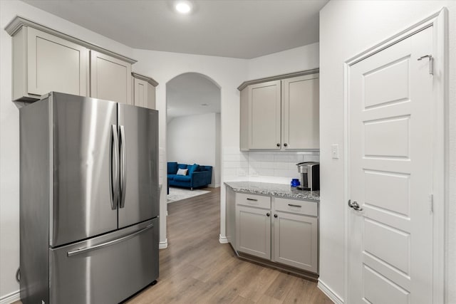 kitchen with decorative backsplash, light wood-style floors, arched walkways, gray cabinetry, and freestanding refrigerator