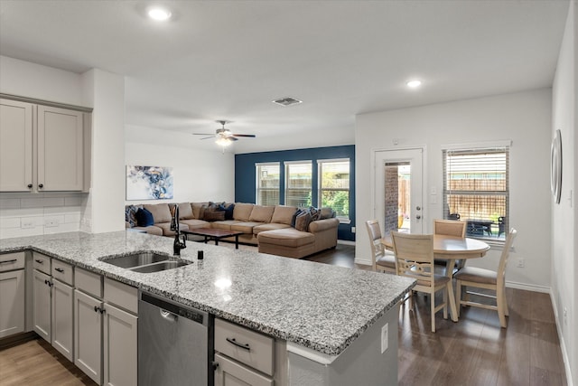 kitchen featuring wood finished floors, stainless steel dishwasher, a sink, light stone countertops, and a peninsula