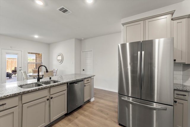 kitchen featuring light stone counters, a sink, light wood-type flooring, stainless steel appliances, and visible vents