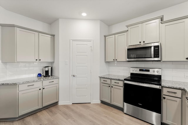 kitchen with light wood-style flooring, appliances with stainless steel finishes, decorative backsplash, and gray cabinetry
