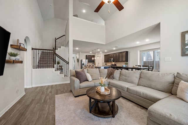 living area featuring stairway, wood finished floors, ceiling fan, a high ceiling, and recessed lighting