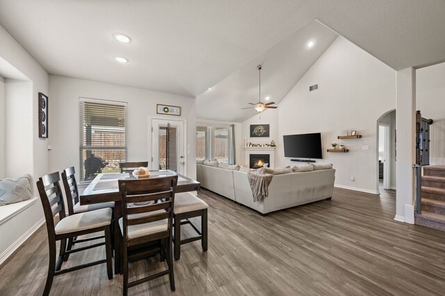 dining area featuring arched walkways, a healthy amount of sunlight, visible vents, ceiling fan, and a lit fireplace