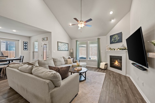 living area featuring plenty of natural light, a glass covered fireplace, dark wood-type flooring, and ceiling fan