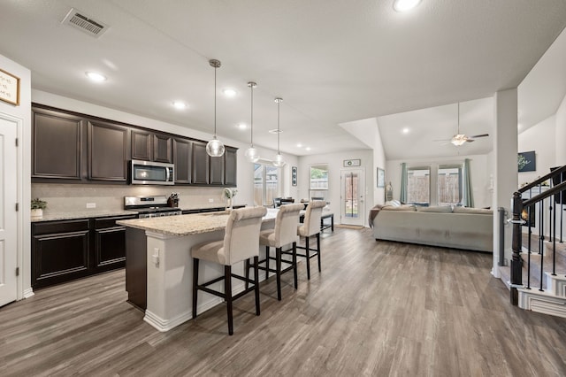 kitchen featuring a kitchen breakfast bar, wood finished floors, visible vents, a kitchen island with sink, and appliances with stainless steel finishes