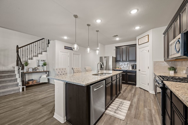 kitchen with stainless steel appliances, a sink, tasteful backsplash, visible vents, and an island with sink