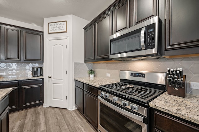 kitchen with decorative backsplash, light wood-style floors, dark brown cabinetry, stainless steel appliances, and light stone countertops