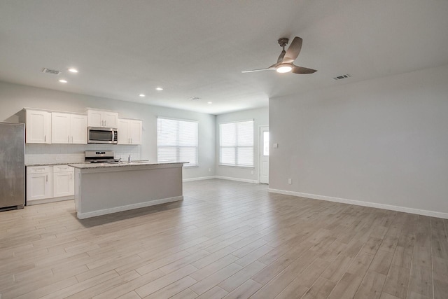 kitchen featuring decorative backsplash, a ceiling fan, appliances with stainless steel finishes, white cabinets, and open floor plan