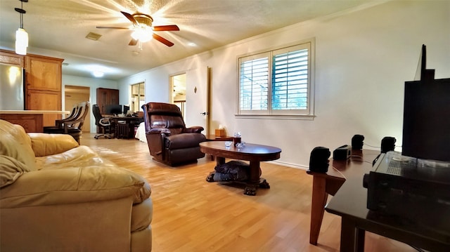 living room featuring light wood finished floors, a ceiling fan, and ornamental molding