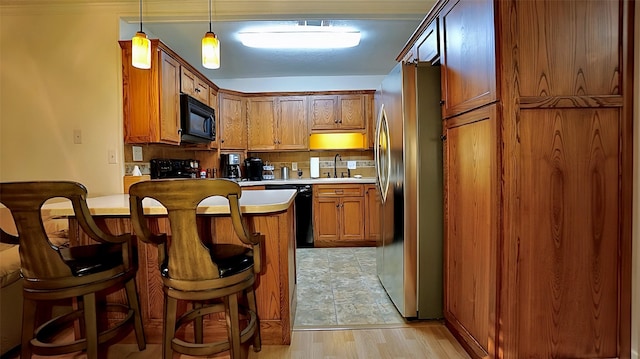 kitchen with a kitchen breakfast bar, light countertops, a sink, black appliances, and brown cabinetry