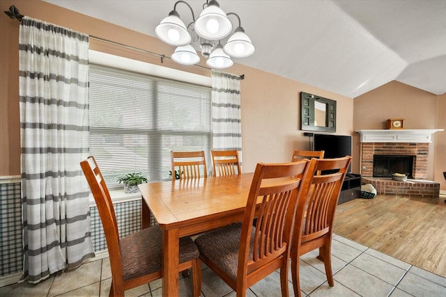 dining area with vaulted ceiling, a brick fireplace, a notable chandelier, and light tile patterned flooring