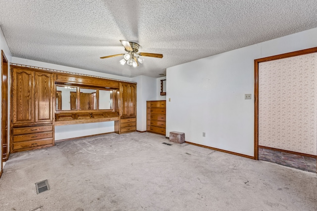 unfurnished bedroom with a textured ceiling, ceiling fan, light colored carpet, baseboards, and visible vents