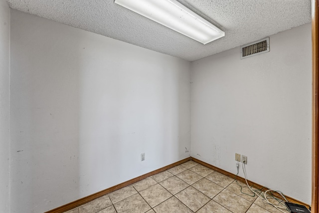 empty room featuring baseboards, visible vents, a textured ceiling, and light tile patterned floors