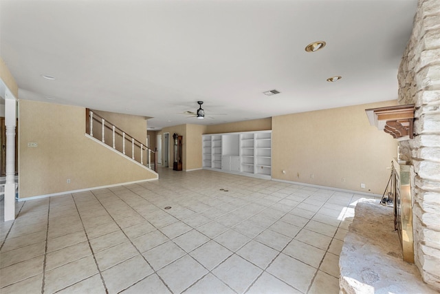 unfurnished living room featuring stairway, a stone fireplace, a ceiling fan, light tile patterned floors, and baseboards