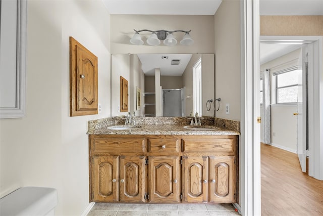 bathroom featuring a shower with shower door, double vanity, toilet, and a sink