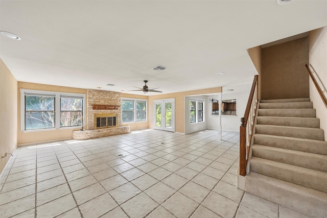 unfurnished living room with stairway, visible vents, light tile patterned floors, a fireplace, and ceiling fan