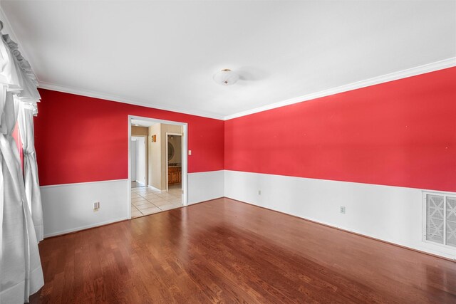 spare room with baseboards, crown molding, wood finished floors, and visible vents