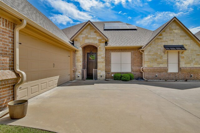1601 Harbor Lakes Dr, Granbury, TX 76048 - french provincial home with stone siding, concrete driveway, a shingled roof, roof mounted solar panels, and brick siding