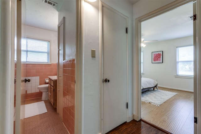 hall with wood finished floors, visible vents, a wainscoted wall, and a healthy amount of sunlight