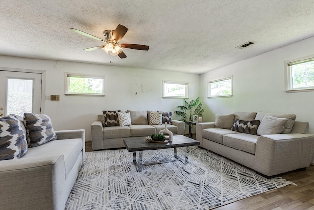 living area with a textured ceiling, wood finished floors, visible vents, and ceiling fan