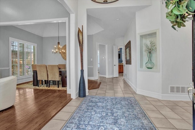tiled entryway with baseboards, visible vents, and a chandelier