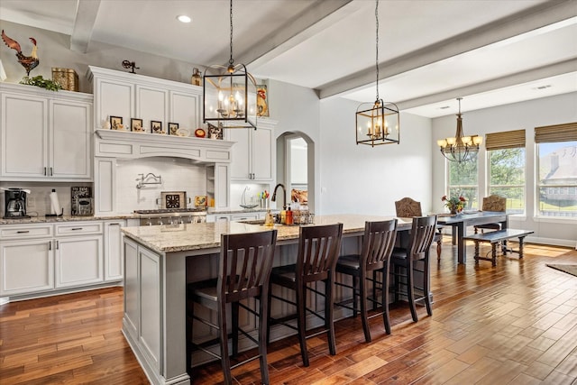 kitchen with tasteful backsplash, arched walkways, white cabinetry, a notable chandelier, and beam ceiling