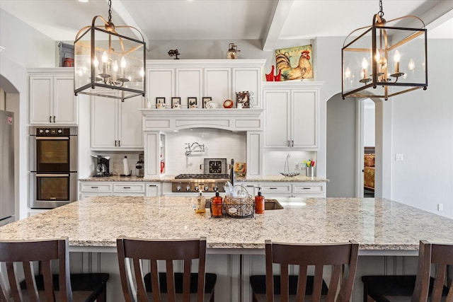 kitchen featuring a large island with sink, arched walkways, backsplash, a notable chandelier, and appliances with stainless steel finishes