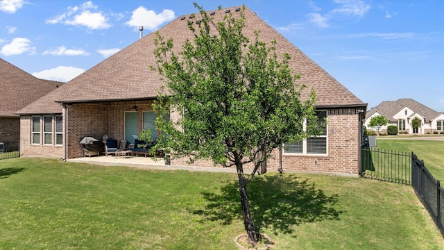 rear view of property with roof with shingles, a fenced backyard, brick siding, a patio area, and a yard