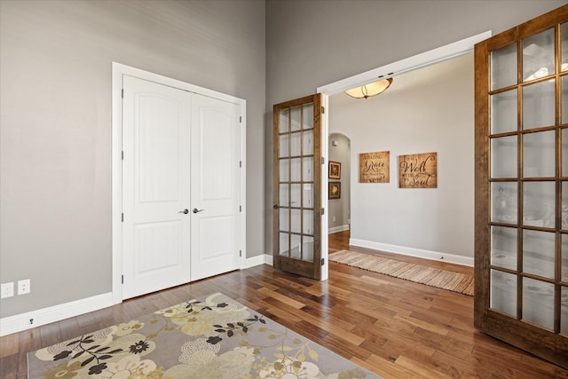 foyer with a towering ceiling, wood finished floors, french doors, arched walkways, and baseboards