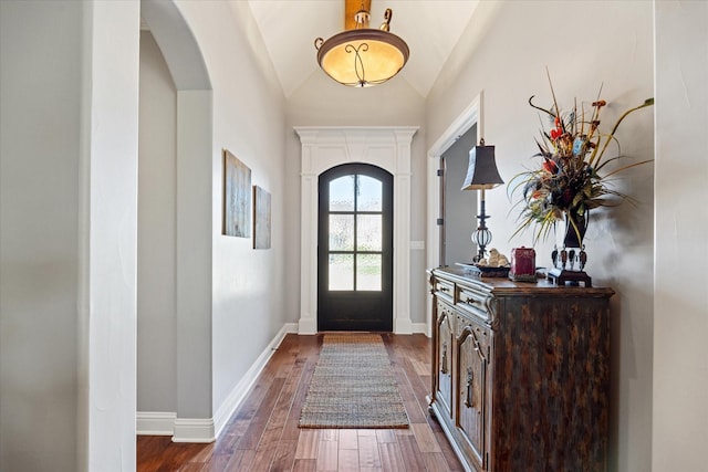 doorway featuring arched walkways, dark wood-style flooring, vaulted ceiling, and baseboards