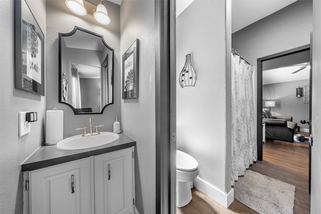 full bath with toilet, wood finished floors, vanity, a textured wall, and baseboards