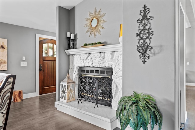 living room featuring baseboards, a stone fireplace, and wood finished floors