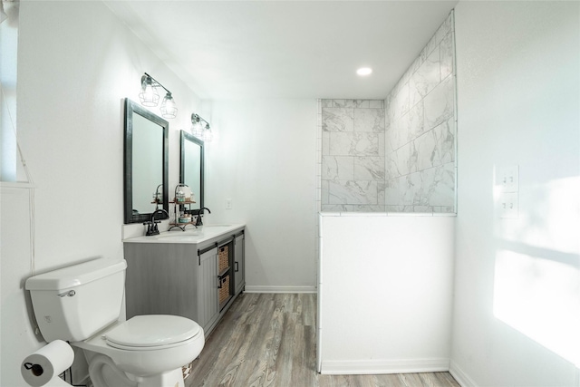 bathroom featuring wood finished floors, toilet, vanity, a walk in shower, and baseboards