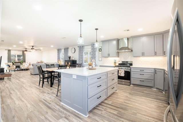 kitchen with wall chimney exhaust hood, light wood-style floors, gray cabinets, a breakfast bar, and appliances with stainless steel finishes