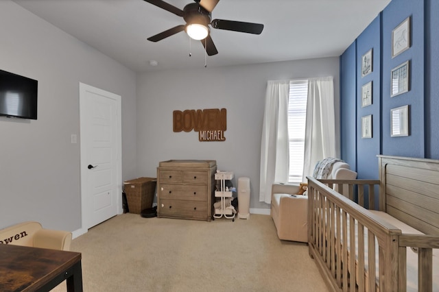 bedroom featuring a nursery area, light carpet, a ceiling fan, and baseboards