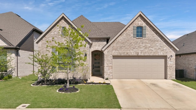 french provincial home with a garage, brick siding, a front yard, and concrete driveway