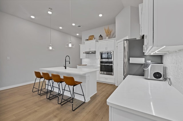 1373 Silverthorn Trl, Justin, TX 76247 - kitchen featuring appliances with stainless steel finishes, under cabinet range hood, a breakfast bar, tasteful backsplash, and a center island with sink