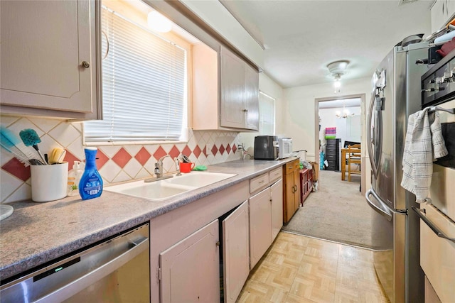 kitchen with a sink, appliances with stainless steel finishes, a chandelier, light countertops, and backsplash
