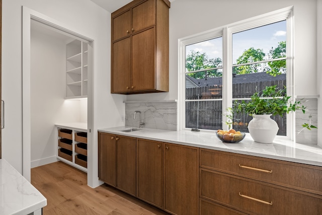 bar featuring light wood-type flooring, a sink, and backsplash