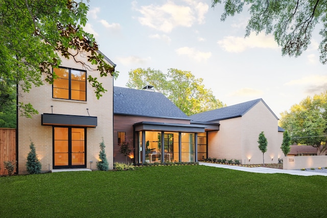 rear view of house featuring fence, brick siding, a lawn, a shingled roof, and a sunroom