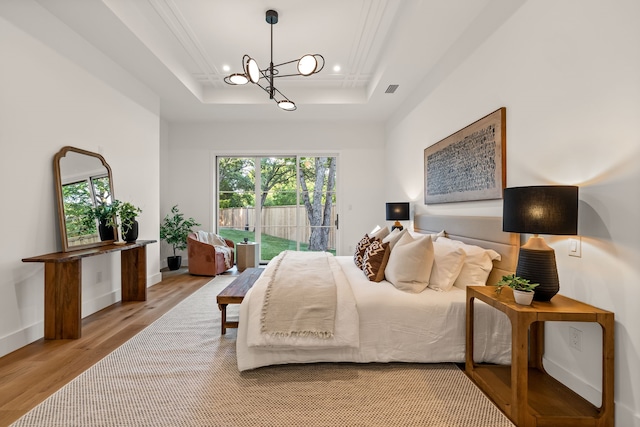bedroom with a tray ceiling, recessed lighting, a chandelier, wood finished floors, and access to outside