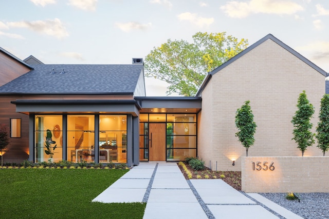 back of property featuring brick siding, a yard, and roof with shingles