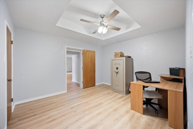 office space featuring baseboards, light wood-style flooring, a tray ceiling, and ceiling fan