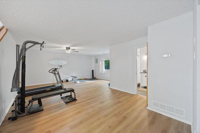 workout area with a textured ceiling, ceiling fan, light wood finished floors, baseboards, and visible vents