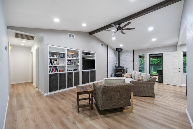 living area featuring a wood stove, vaulted ceiling with beams, a ceiling fan, and visible vents
